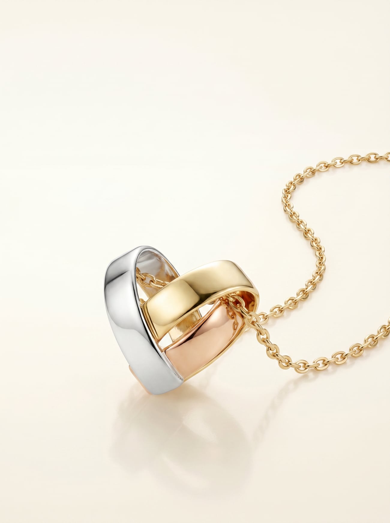 Der gefaltete Tri-Gold-Herzanhänger im Detail: Weißgold, Gelbgold und Roségold kreuzen sich poliert in der Herzform.